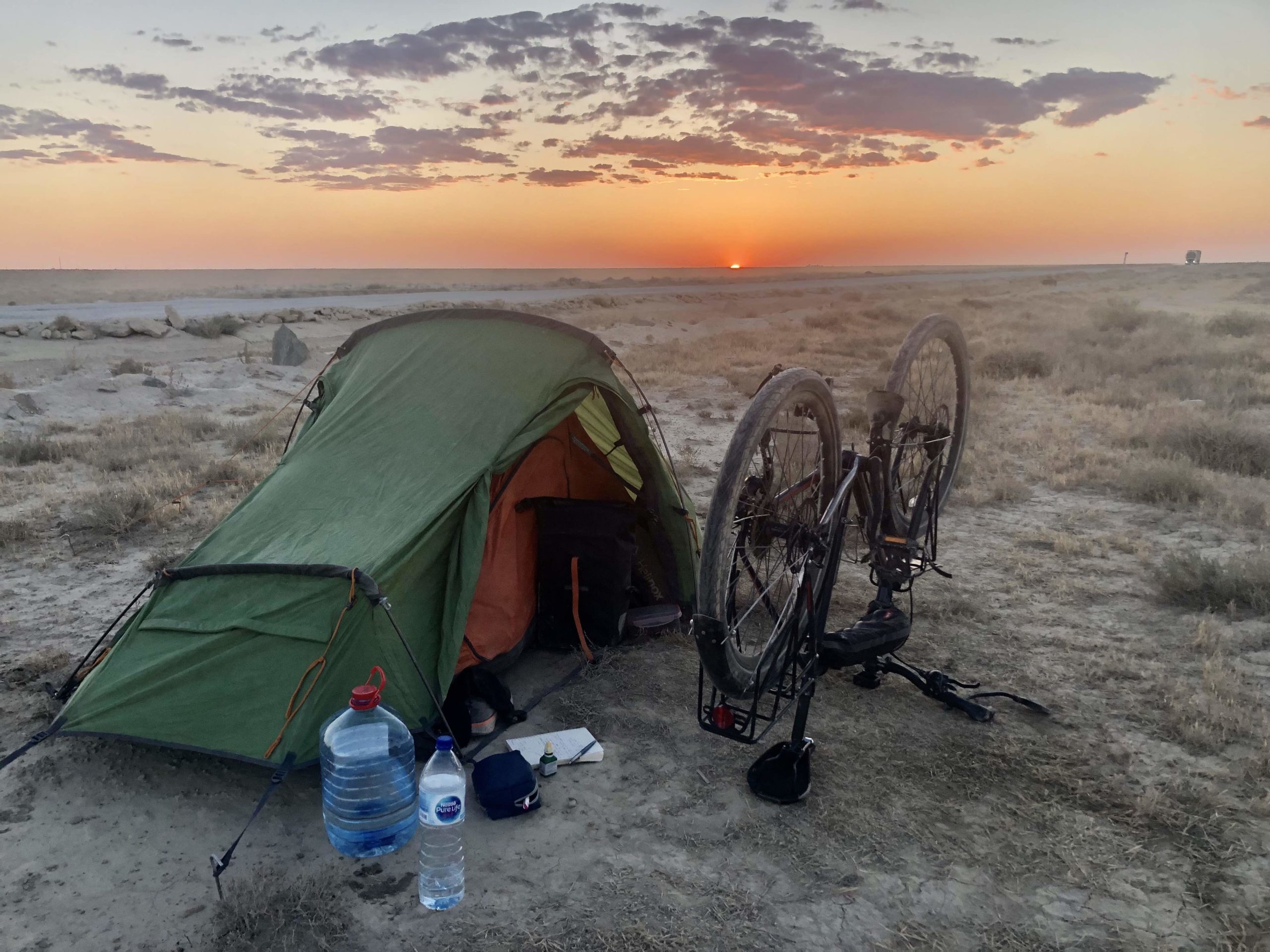 A photograph of a tent and bike pitched for the night on dry terrain at sunset, for Matt Spencer’s cycling for sturgeon journey.