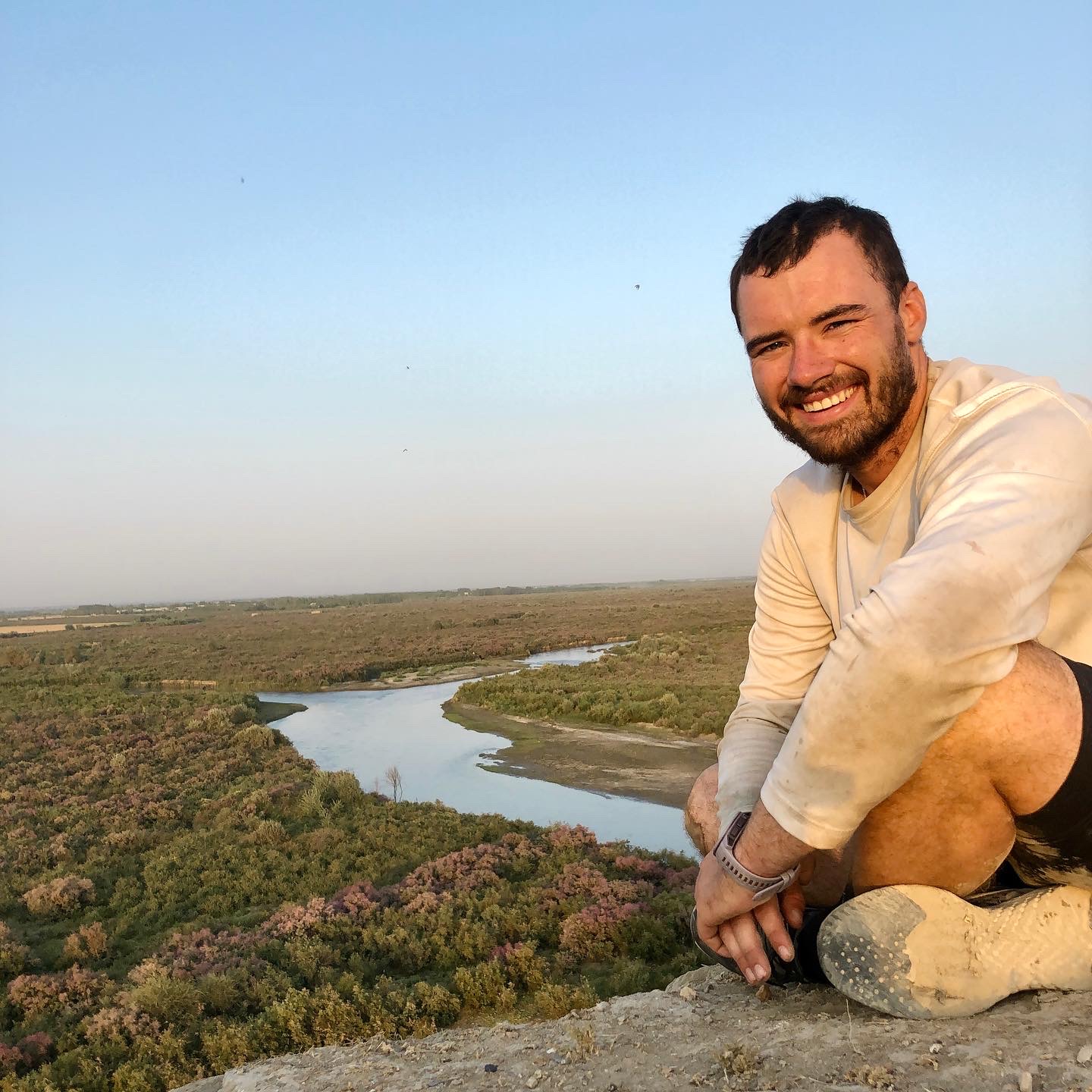 A photograph of Matt Spencer sitting on a rock with a view of a river behind him on his cycling for sturgeon journey.