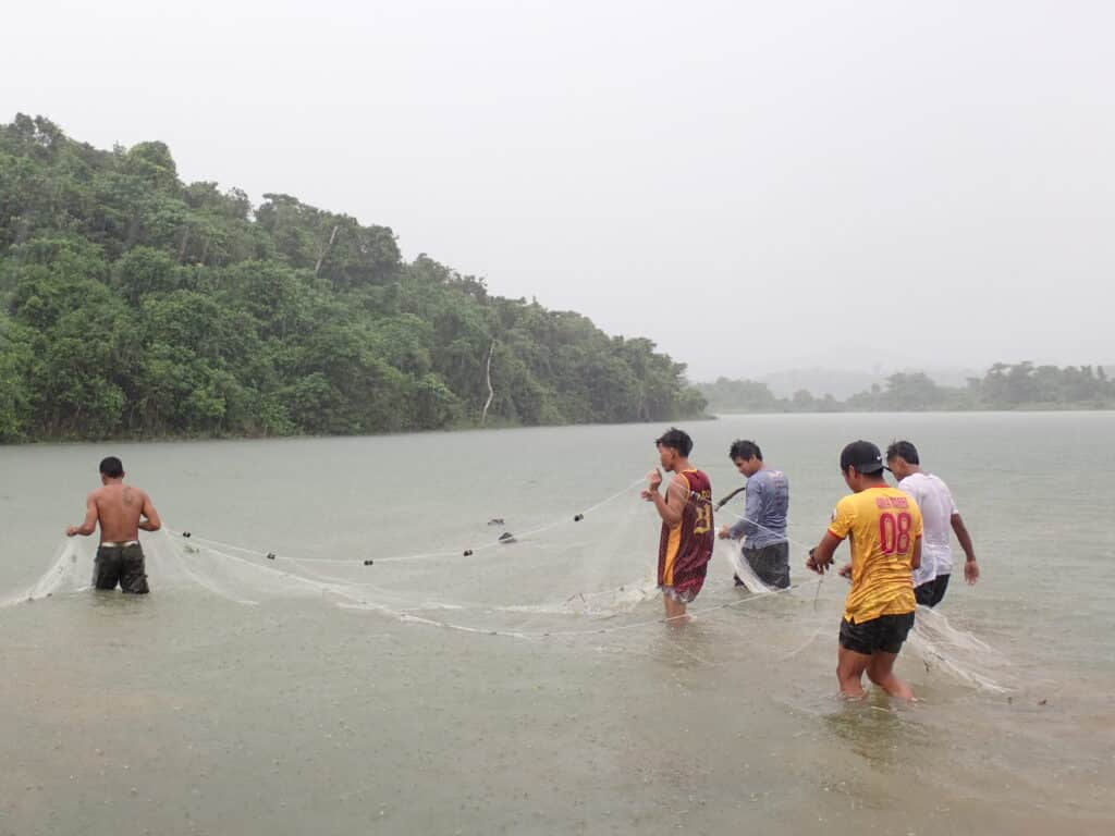 Four men standing in a lake holdng a large fishing net between them.