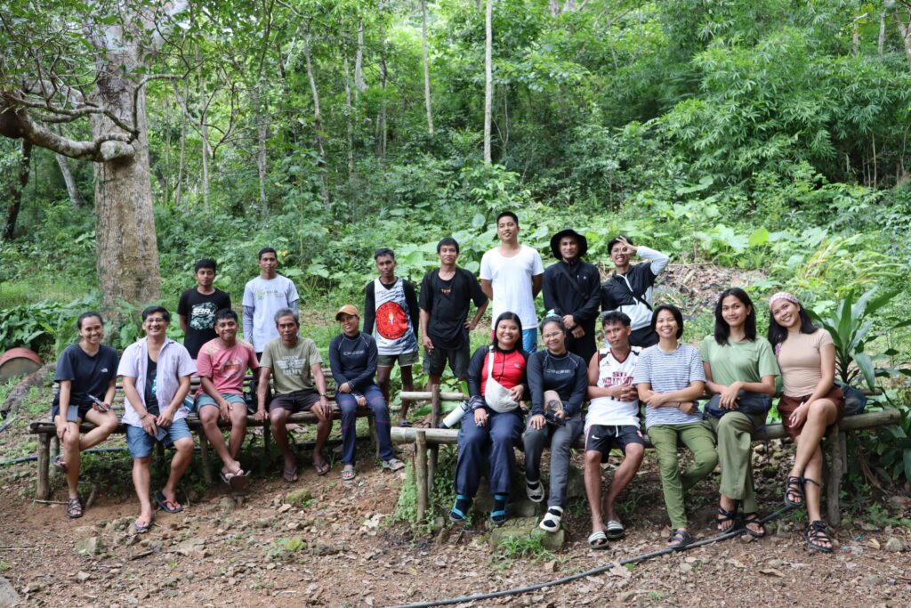 Eighteen people sitting in the forest and smiling at the camera,