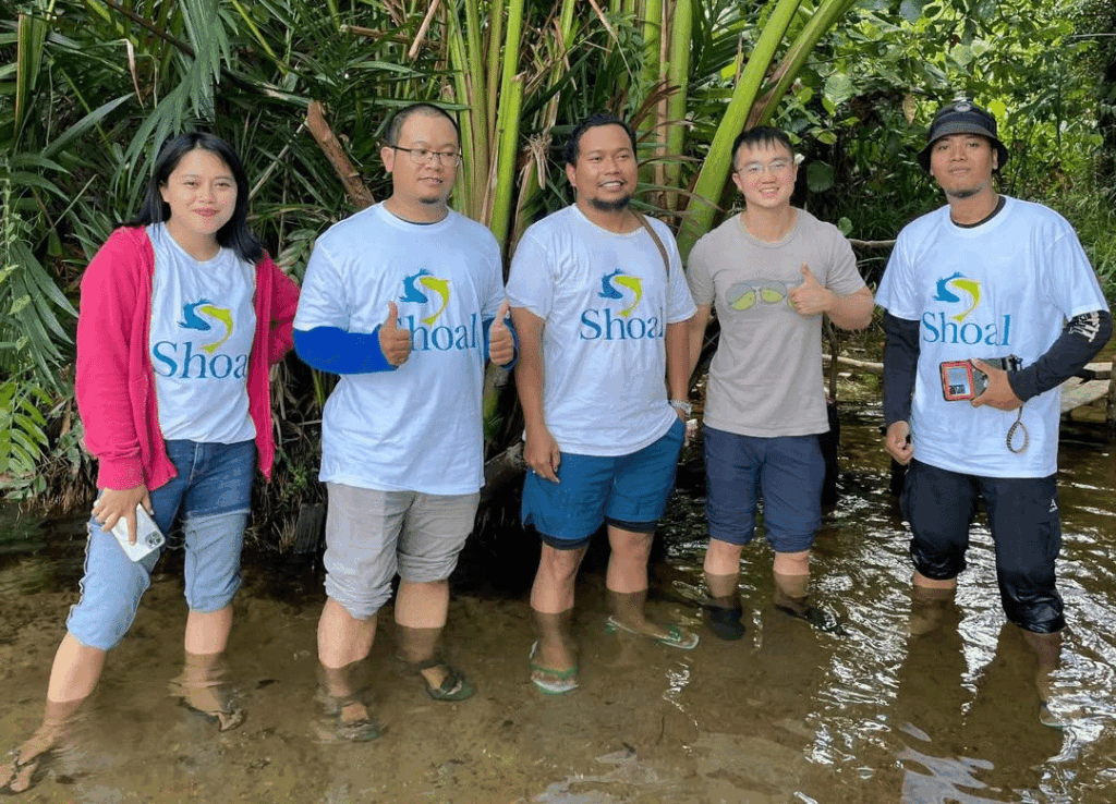Five people knee deep in water smiling at the camera wearing SHOAL shirts.