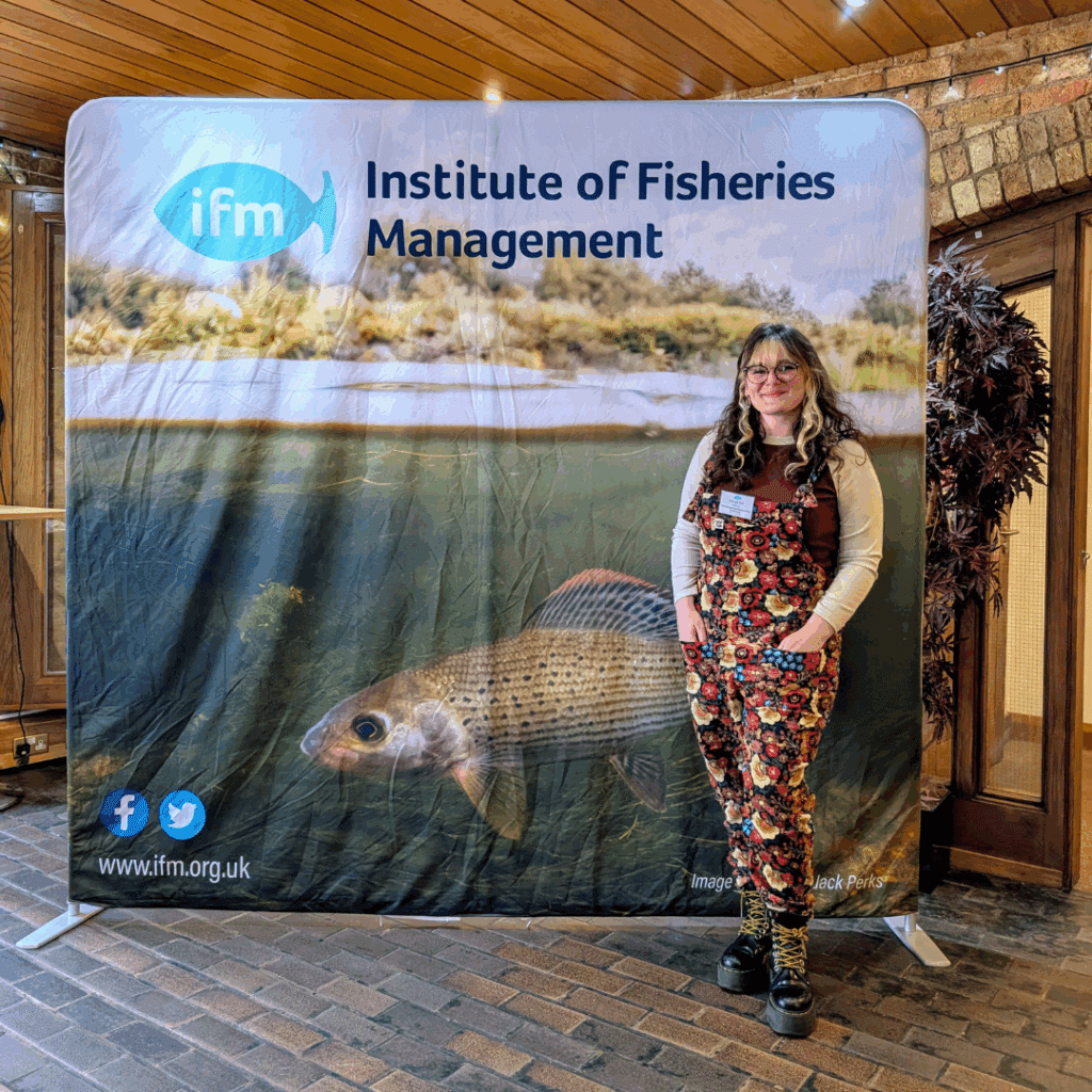 SHOAL's programme officer Georgie Bull standing in front of a banner for the Institute of Fisheries Management.